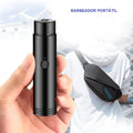 Hand holding a black portable rechargeable electric shaver with power button, travel setting