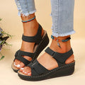 Black comfort wedge sandals for women with velcro straps, worn with ripped jeans.