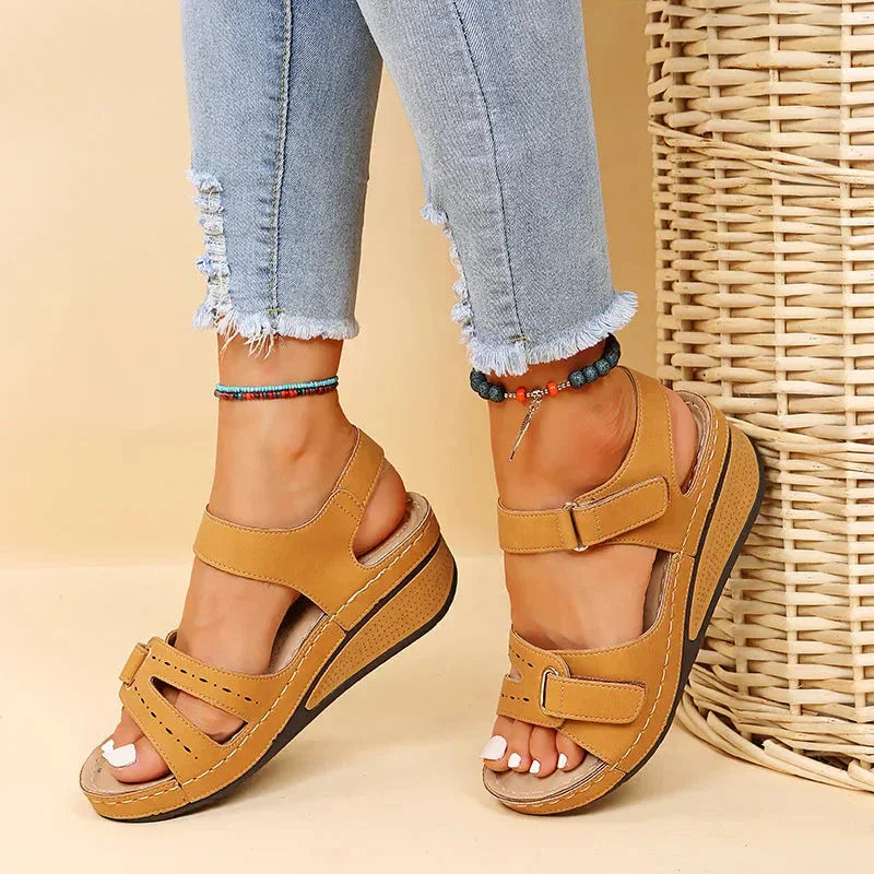 Woman wearing tan comfort wedge sandals with velcro straps and frayed hem jeans