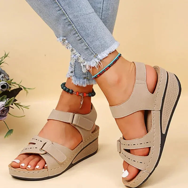 Beige comfort wedge sandals for women with velcro straps, worn with frayed jeans.