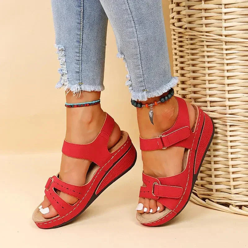 Red comfort wedge sandals for women with double straps and buckles, worn with jeans.