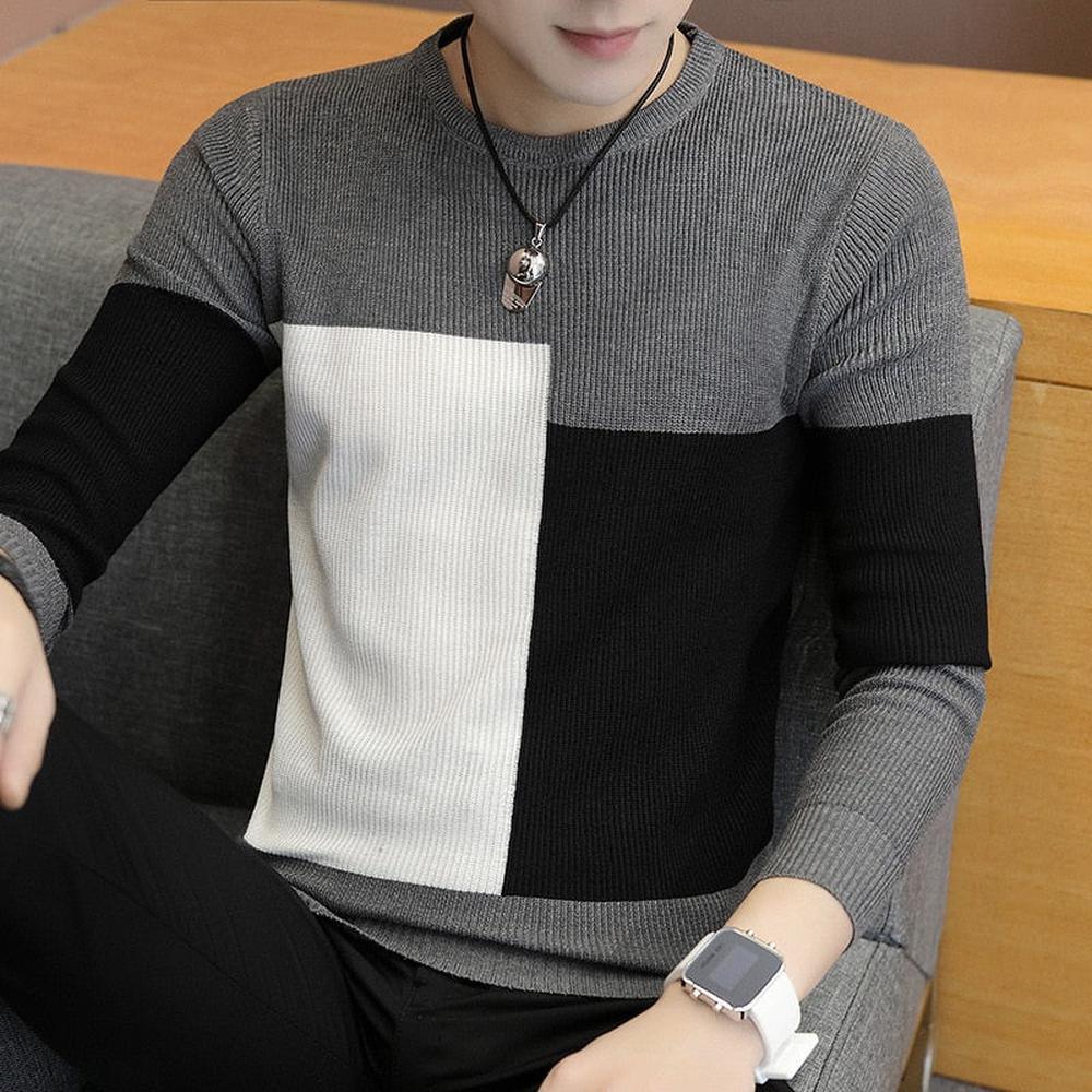 Man wearing colorblock knit sweater in gray, black, and white, sitting on a couch